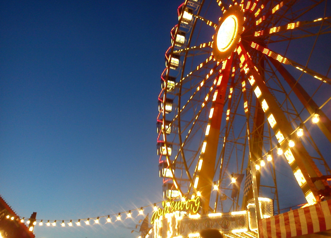 A brightly lit ferris wheel at a festival at dusk.